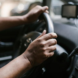Hände einer Person am Lenkrad im Innenraum eines Fahrzeugs.