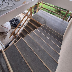 Außentreppe mit grauem Unterbodenbelag und Holzgeländer während Bauarbeiten.