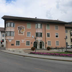 Gebäude mit rosafarbener, teilweise bemalter Fassade und Eingangsbogen an einer Straße.