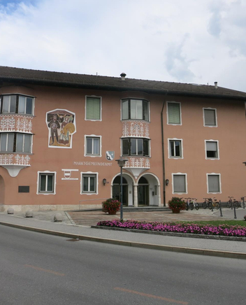 Gebäude mit rosafarbener, teilweise bemalter Fassade und Eingangsbogen an einer Straße.