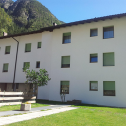 Großes Gebäude mit weißer Fassade, einem Rasen davor und Berglandschaft im Hintergrund.