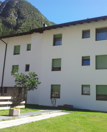 Grande edificio con facciata bianca, un prato davanti e un paesaggio montano sullo sfondo.